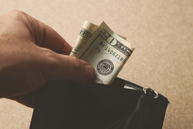 Closeup shot of a person putting some money in his leather wallet Closeup of man putting dollar bill in wallet illustrates blog "Economic Control: A Lesser-Known Aspect of Domestic Abuse"