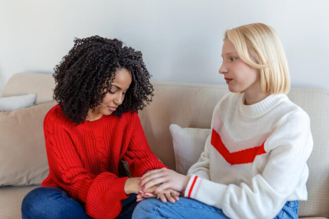 friend-trying-calm-down-her-friend-woman-crying-young-lady-sharing-her-problem-with-friend-female-depression-woman-omforting-hes-sad-friend-sitting-couch-living-room-home Woman comforting a friend while discussing domestic abuse support